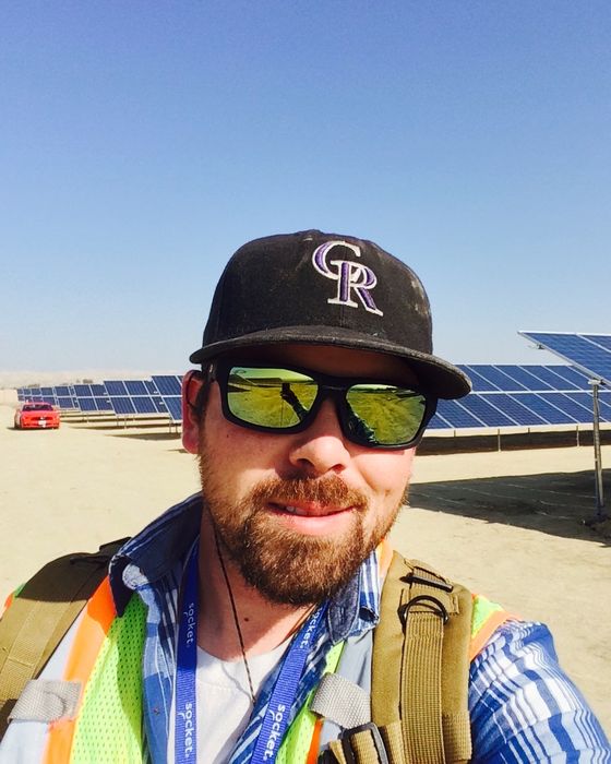 Selfie in sunglasses and a safety vest, a single-axis tracker row and desert behind.
