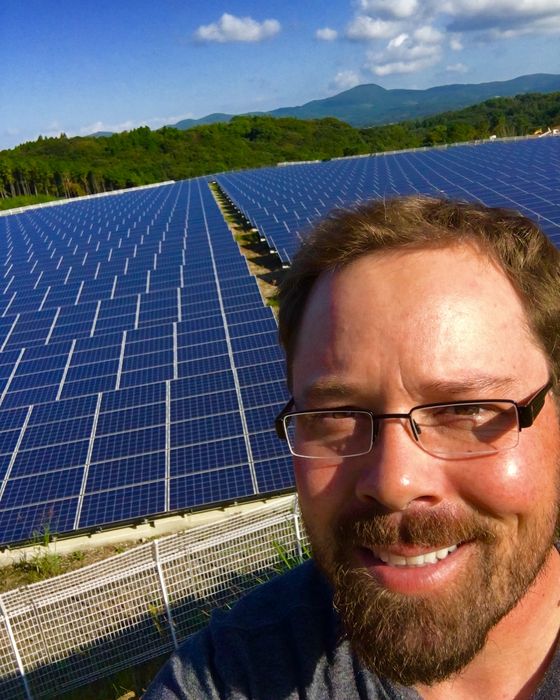 Selfie in front of a large hillside array with green mountains beyond.
