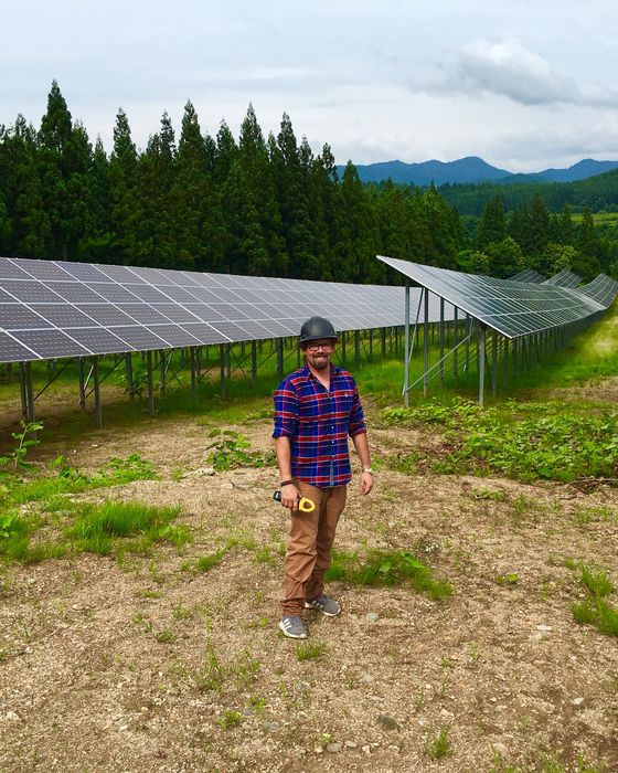 Standing between two long array rows with a cedar forest and mountains behind.