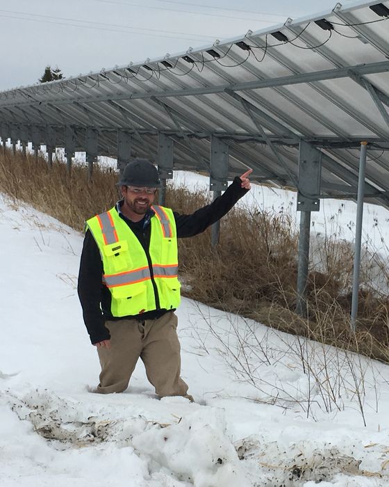 Knee-deep in snow, pointing up at the underside of a fixed-tilt array.