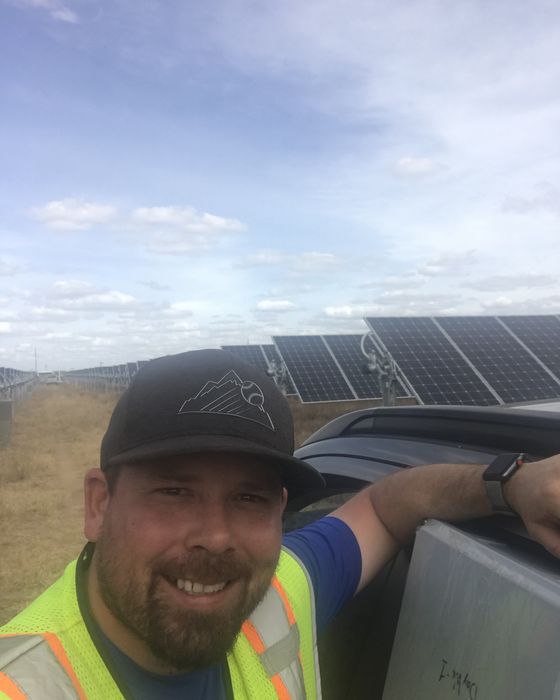 Selfie leaning on a truck beside tracker rows on dry grassland.