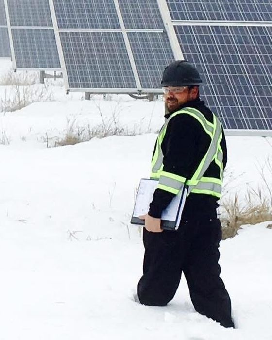 Walking through deep snow with a clipboard beside a fixed-tilt array.