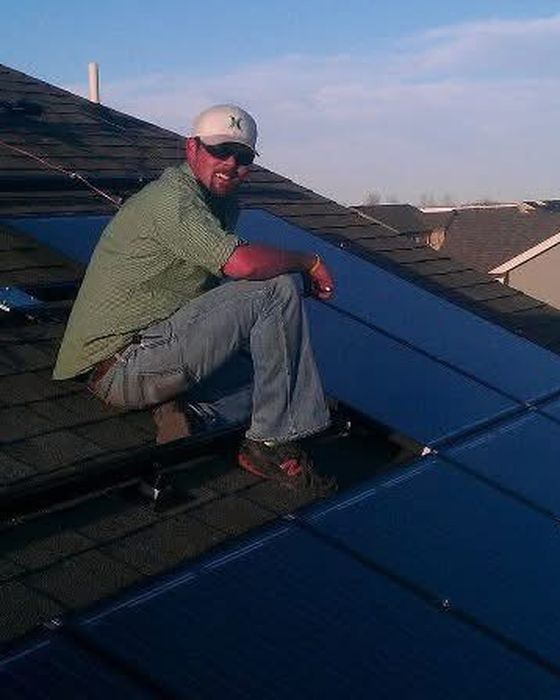 Kneeling on a shingle roof beside newly installed black panels.